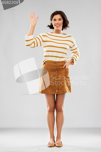 Image of woman in pullover, skirt and shoes waving hand