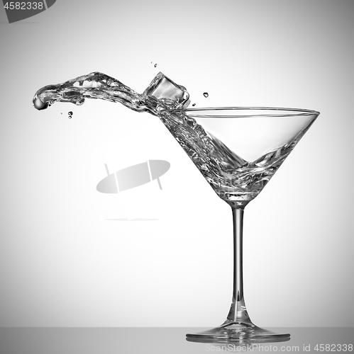 Image of Clear cocktail splash out of glass with ice cube.