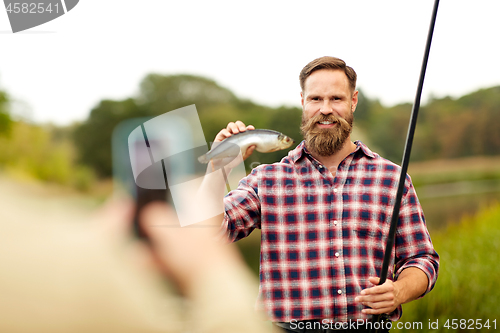 Image of friend photographing fisherman with fish at lake