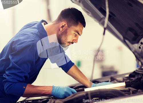 Image of mechanic man with lamp repairing car at workshop