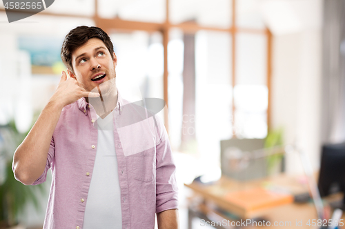 Image of man showing phone call gesture over office room