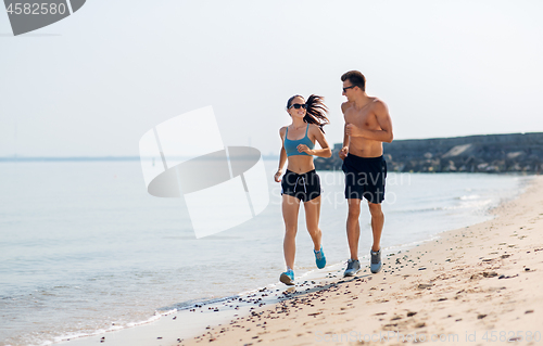 Image of couple in sports clothes running along on beach