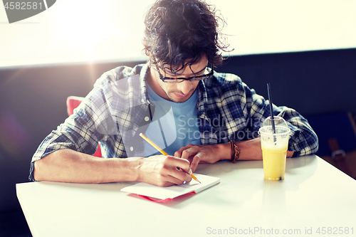 Image of man with notebook and juice writing at cafe