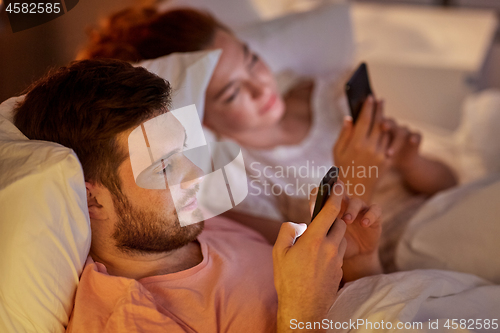 Image of couple using smartphones in bed at night