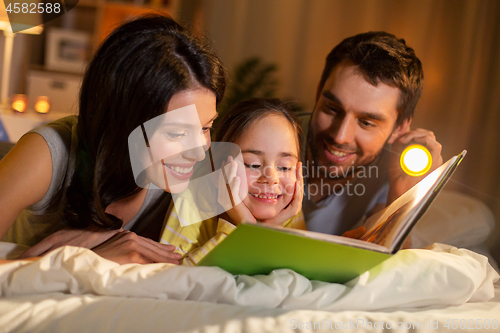 Image of happy family reading book in bed at night at home