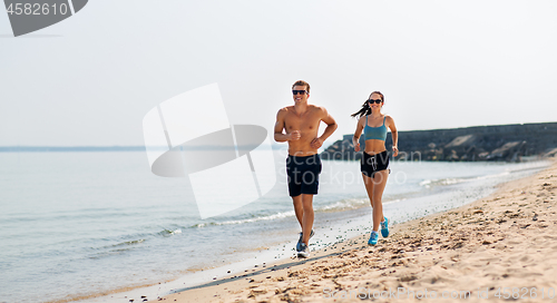 Image of couple in sports clothes running along on beach