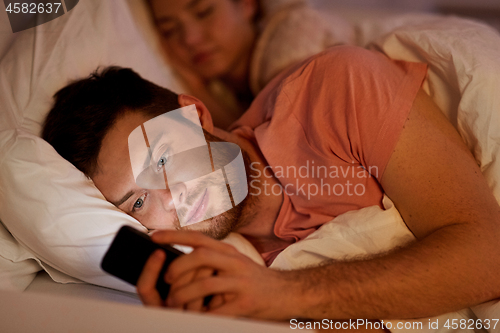 Image of man using smartphone while girlfriend is sleeping