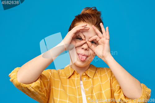 Image of red haired teenage girl making finger glasses