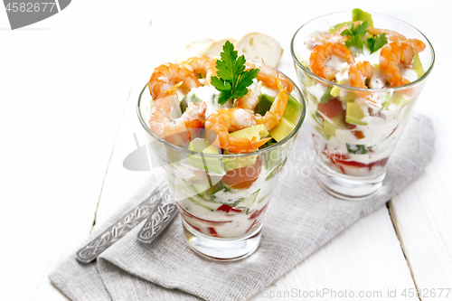 Image of Salad with shrimp and avocado in two glasses on light board