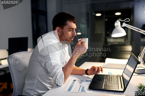 Image of businessman with coffee and laptop at night office