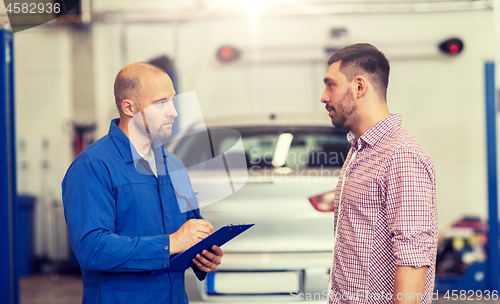 Image of auto mechanic with clipboard and man at car shop