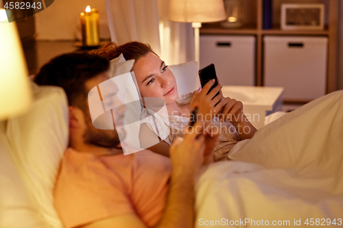 Image of couple using smartphones in bed at night