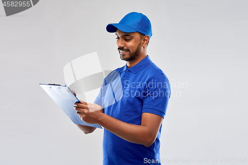 Image of happy indian delivery man with clipboard in blue