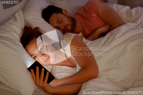 Image of woman using smartphone while boyfriend is sleeping