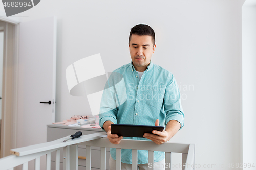 Image of father with tablet pc assembling baby bed at home