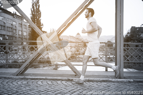 Image of man jogging across the bridge at sunny morning