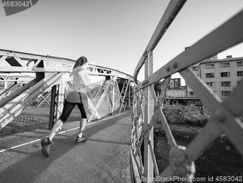 Image of woman jogging across the bridge at sunny morning