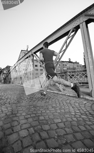 Image of man jogging across the bridge at sunny morning