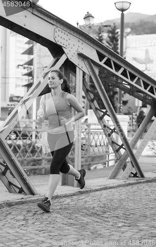 Image of woman jogging across the bridge at sunny morning