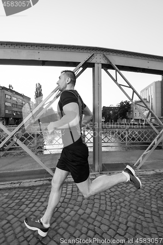 Image of man jogging across the bridge at sunny morning