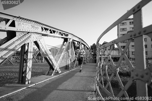 Image of woman jogging across the bridge at sunny morning