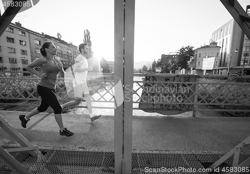 Image of young couple jogging across the bridge in the city