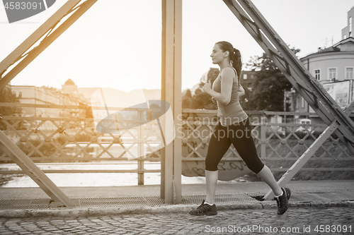 Image of woman jogging across the bridge at sunny morning