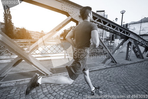 Image of man jogging across the bridge at sunny morning