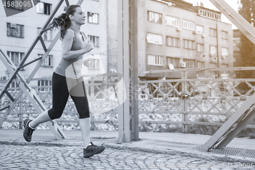 Image of woman jogging across the bridge at sunny morning