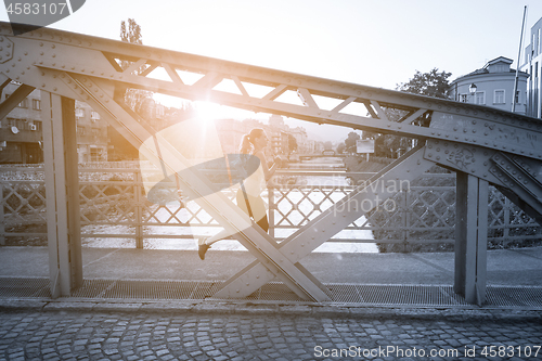 Image of woman jogging across the bridge at sunny morning