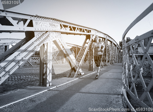 Image of woman jogging across the bridge at sunny morning