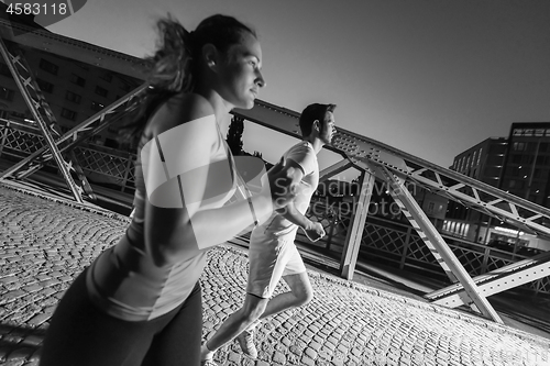 Image of couple jogging across the bridge in the city