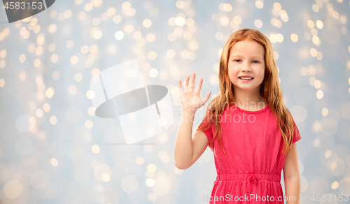 Image of smiling red haired girl waving hand over lights