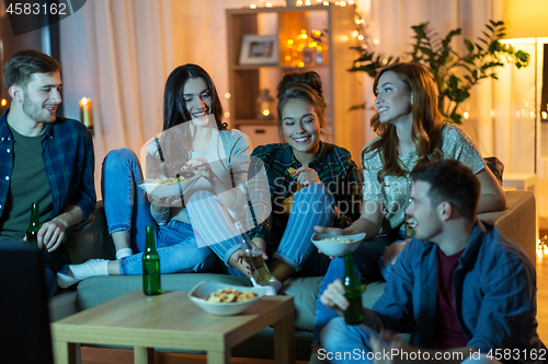 Image of friends with drinks and snacks watching tv at home