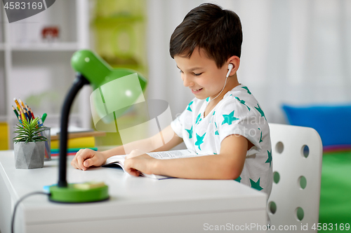 Image of student boy in earphones reading book at home