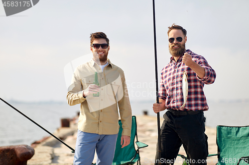 Image of happy friends with fishing rods and beer on pier