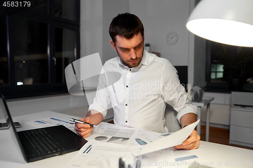 Image of businessman with papers and laptop at night office