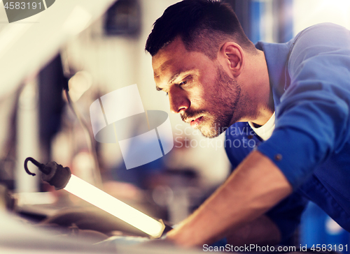 Image of mechanic man with lamp repairing car at workshop