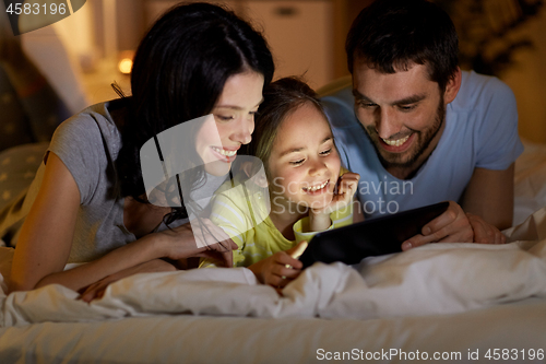 Image of family with tablet pc in bed at night at home