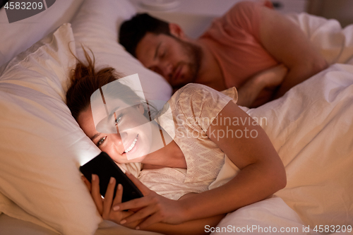 Image of woman using smartphone while boyfriend is sleeping