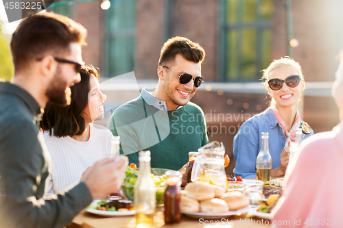 Image of happy friends eating and drinking at rooftop party