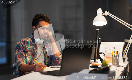 Image of creative man with laptop working at night office