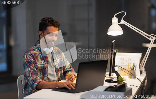 Image of creative man with laptop working at night office