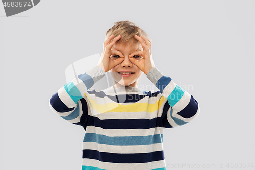 Image of boy in pullover looking through finger glasses