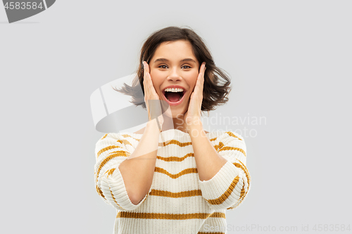 Image of impressed woman in pullover holding to her face