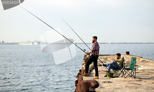 Image of happy friends with fishing rods on pier