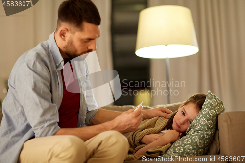 Image of father with thermometer and ill daughter at home