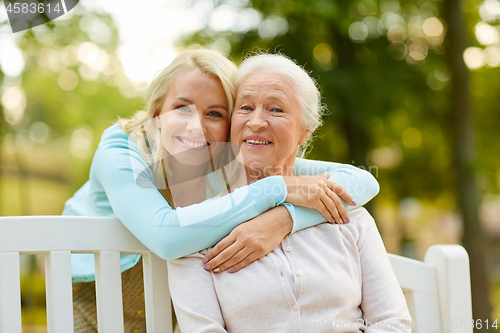 Image of daughter with senior mother hugging on park bench