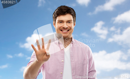 Image of young man showing four fingers over sky