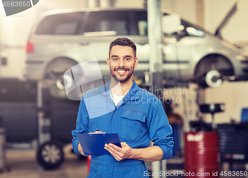 Image of happy mechanic man with clipboard at car workshop